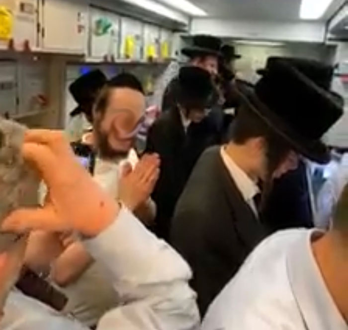 An aircraft galley full of orthodox Jewish men saying prayers