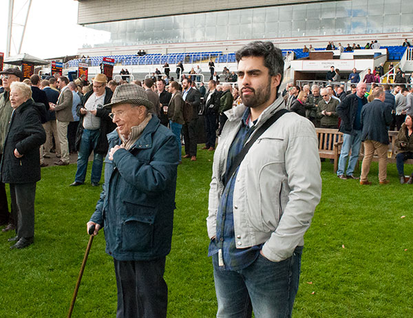 a young and elderly man standing together on the grass with other people behind them