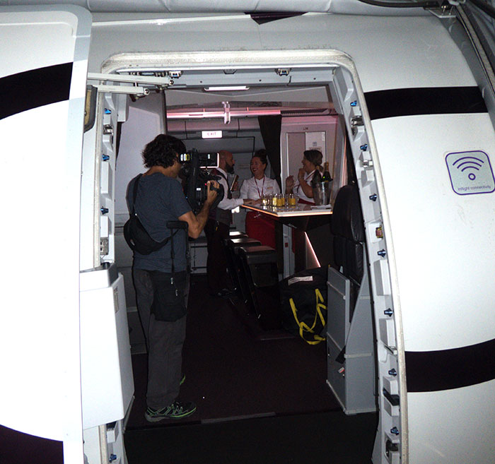 A member of film crew standing inside the aircraft filming three cabin crew