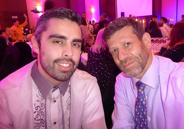 two smartly dressed men smiling for a selfie at some kind of indoor event